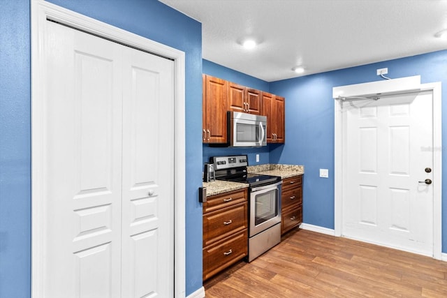 kitchen with light stone countertops, light hardwood / wood-style flooring, and appliances with stainless steel finishes