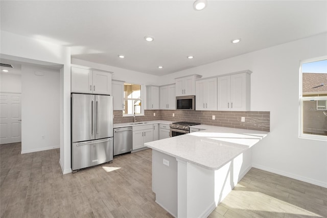 kitchen with sink, stainless steel appliances, backsplash, white cabinets, and light wood-type flooring