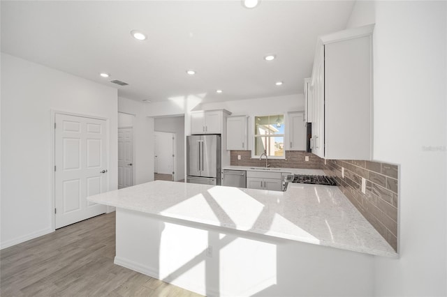 kitchen featuring kitchen peninsula, backsplash, stainless steel appliances, sink, and white cabinetry