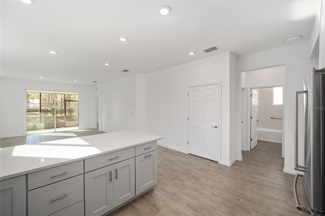 kitchen featuring gray cabinets, stainless steel fridge, light stone counters, and light hardwood / wood-style floors