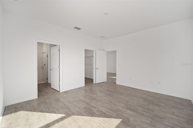 unfurnished bedroom with ensuite bath, a spacious closet, a closet, and light hardwood / wood-style floors