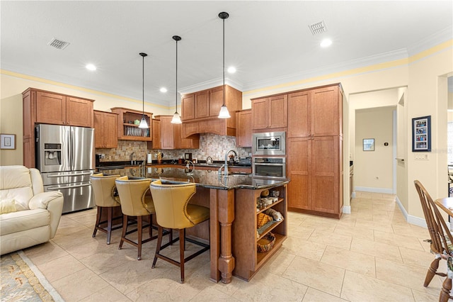 kitchen with hanging light fixtures, backsplash, crown molding, a kitchen island with sink, and appliances with stainless steel finishes