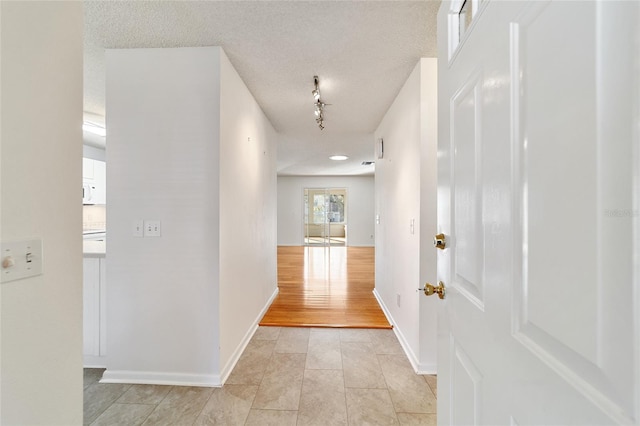 hallway with light tile patterned flooring, track lighting, and a textured ceiling