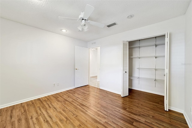 unfurnished bedroom with wood-type flooring, a textured ceiling, a closet, and ceiling fan