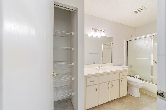 full bathroom featuring enclosed tub / shower combo, tile patterned floors, a textured ceiling, toilet, and vanity