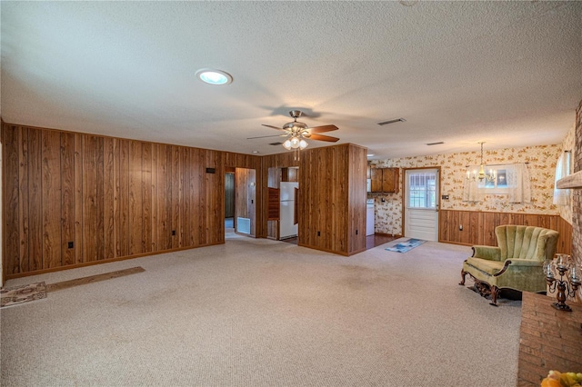 unfurnished living room with wood walls, a brick fireplace, ceiling fan, a textured ceiling, and carpet floors