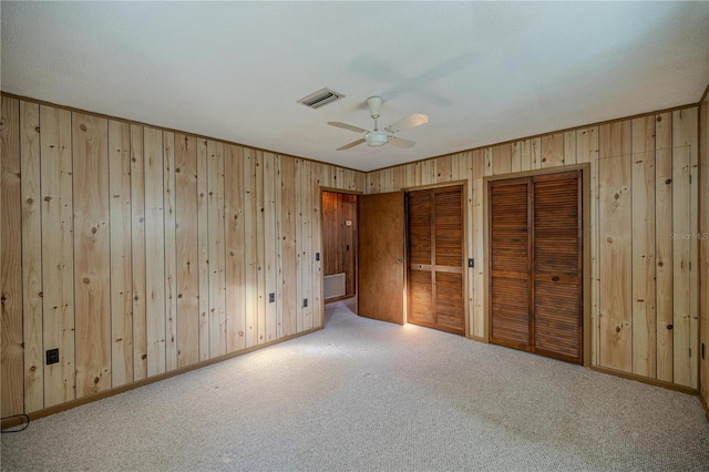 unfurnished bedroom featuring ceiling fan, light carpet, and two closets