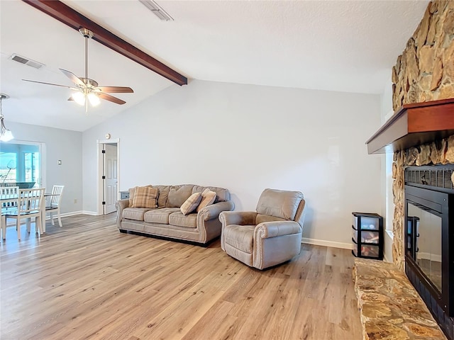 living room featuring lofted ceiling with beams, light hardwood / wood-style floors, a fireplace, and ceiling fan