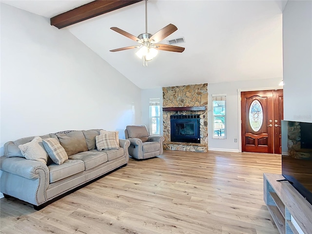 living room featuring light wood-type flooring, a wealth of natural light, ceiling fan, beamed ceiling, and a stone fireplace