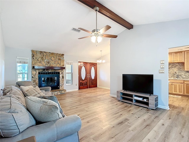 living room featuring light wood-type flooring, lofted ceiling with beams, a stone fireplace, and sink