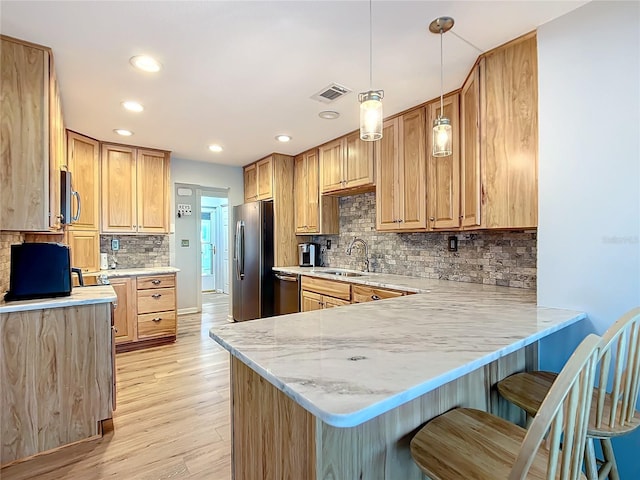 kitchen with kitchen peninsula, appliances with stainless steel finishes, a kitchen breakfast bar, sink, and hanging light fixtures