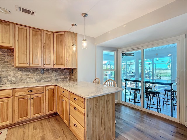 kitchen featuring kitchen peninsula, light stone countertops, hanging light fixtures, and light hardwood / wood-style floors