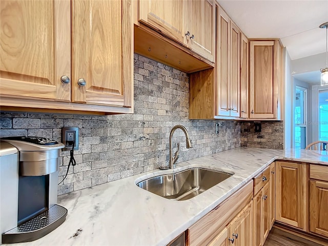 kitchen featuring backsplash, light stone counters, sink, and hanging light fixtures