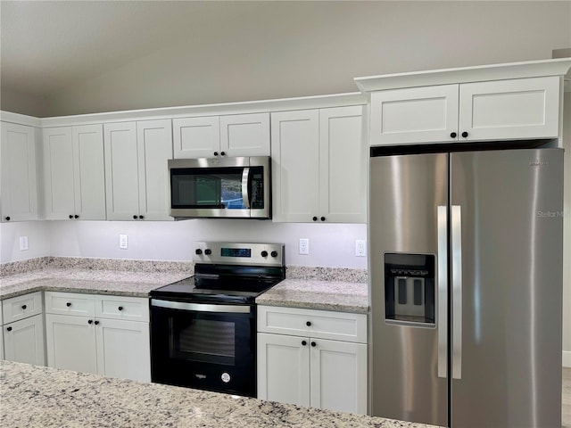 kitchen with light stone countertops, white cabinets, stainless steel appliances, and vaulted ceiling