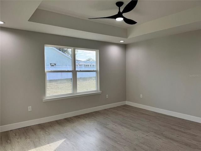 empty room with hardwood / wood-style flooring, ceiling fan, and a raised ceiling