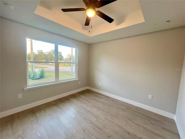 empty room featuring light wood-type flooring, ceiling fan, and a raised ceiling