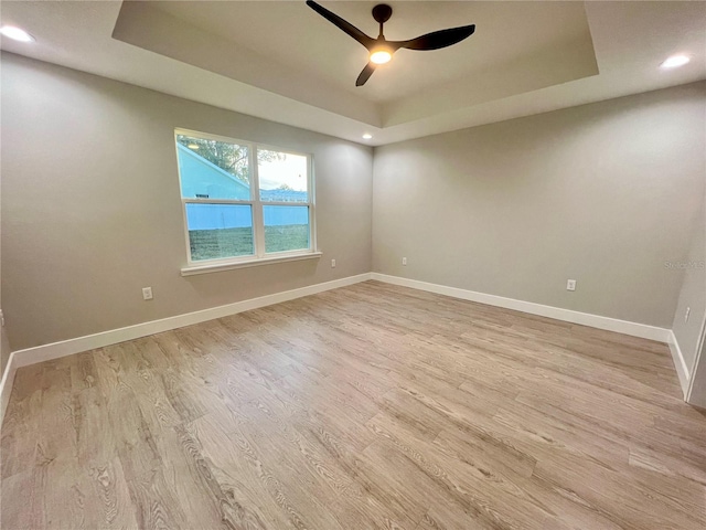 empty room with ceiling fan, light hardwood / wood-style floors, a raised ceiling, and a water view