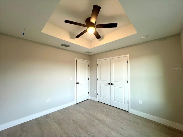 unfurnished bedroom featuring ceiling fan, a closet, light hardwood / wood-style flooring, and a tray ceiling