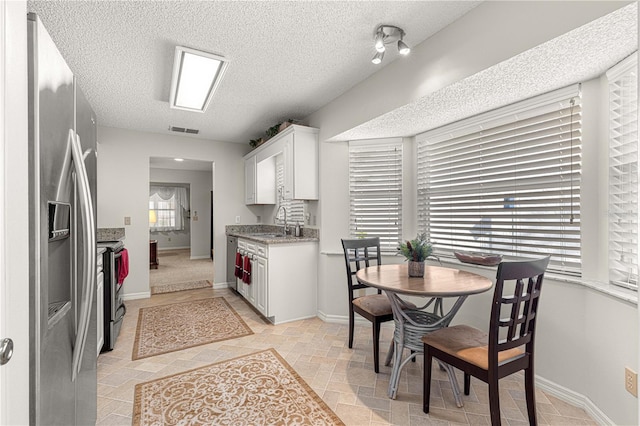 kitchen featuring appliances with stainless steel finishes, light stone counters, a textured ceiling, sink, and white cabinets