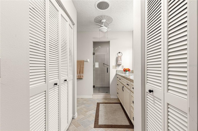 bathroom featuring ceiling fan, vanity, a textured ceiling, and walk in shower