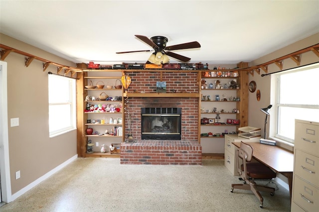 unfurnished office featuring ceiling fan, a wealth of natural light, and a brick fireplace