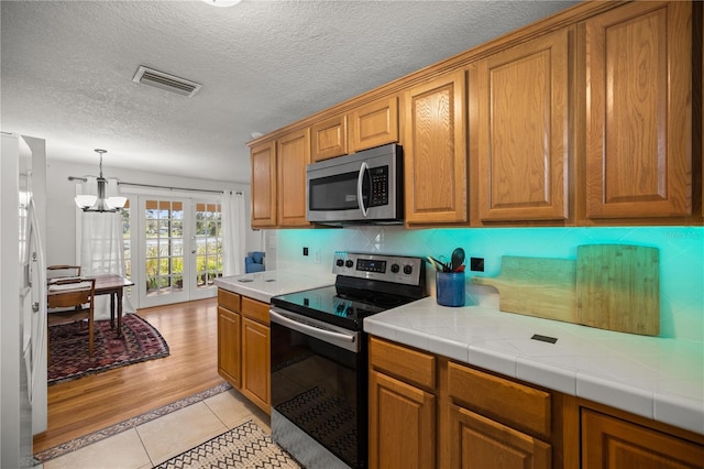 kitchen featuring french doors, tile countertops, a chandelier, light tile patterned floors, and appliances with stainless steel finishes