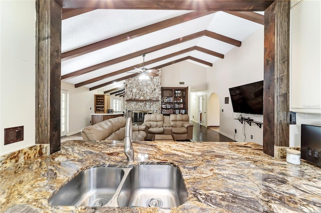 kitchen with a stone fireplace, ceiling fan, sink, and high vaulted ceiling