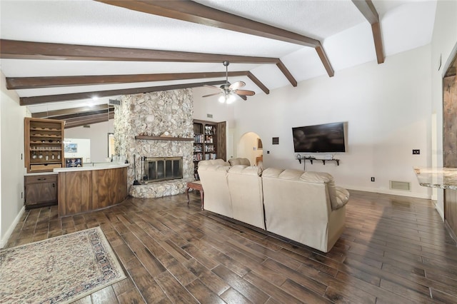 living room with vaulted ceiling with beams, ceiling fan, and a stone fireplace