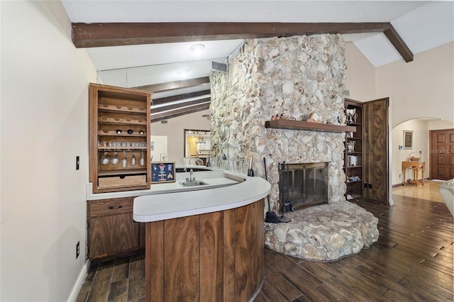 bar with vaulted ceiling with beams, a stone fireplace, dark wood-type flooring, and sink