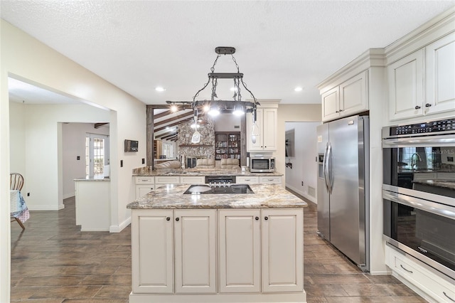 kitchen with decorative backsplash, appliances with stainless steel finishes, light stone counters, a kitchen island, and hanging light fixtures