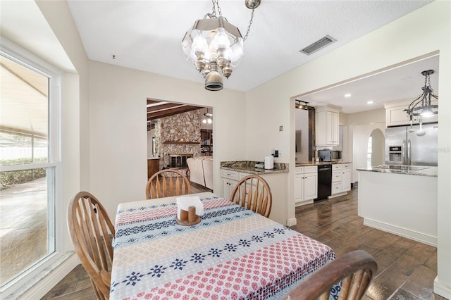 dining area featuring a textured ceiling, a stone fireplace, and a notable chandelier