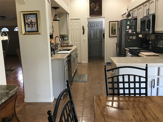 kitchen featuring sink, dark tile patterned floors, kitchen peninsula, decorative light fixtures, and appliances with stainless steel finishes