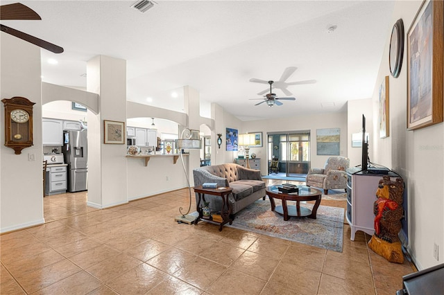 living area featuring visible vents, arched walkways, light tile patterned flooring, and a ceiling fan