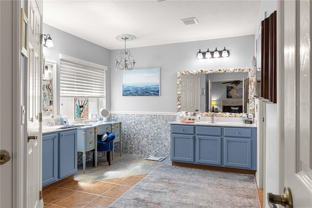 ensuite bathroom with a wainscoted wall, a notable chandelier, ensuite bathroom, a textured ceiling, and vanity