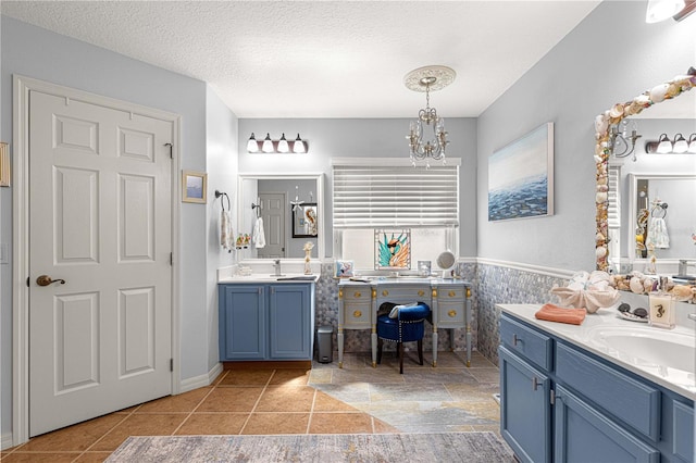 full bathroom featuring wainscoting, a textured ceiling, an inviting chandelier, and two vanities