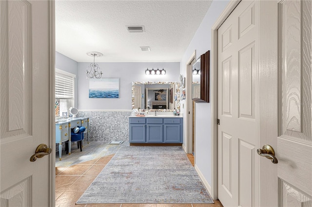 bathroom featuring visible vents, a wainscoted wall, vanity, an inviting chandelier, and a textured ceiling