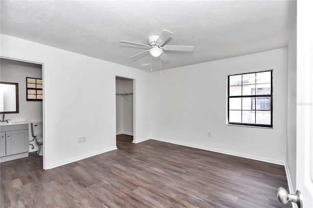 unfurnished bedroom with a walk in closet, ensuite bathroom, a textured ceiling, ceiling fan, and dark wood-type flooring