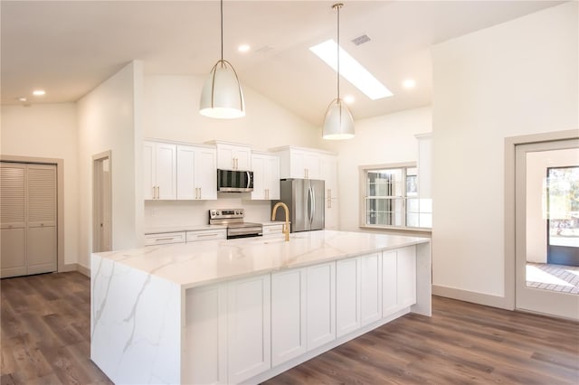 kitchen featuring a skylight, hanging light fixtures, stainless steel appliances, an island with sink, and white cabinets