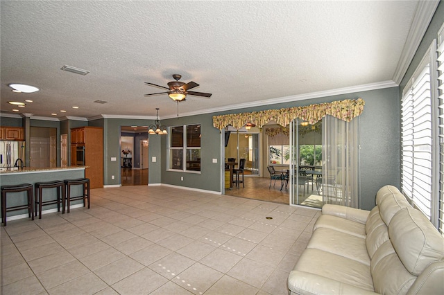 tiled living room with a textured ceiling, ceiling fan with notable chandelier, and crown molding