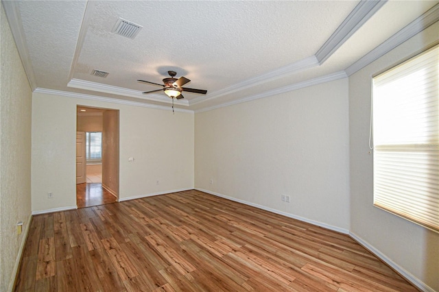 empty room with crown molding, light hardwood / wood-style flooring, ceiling fan, a textured ceiling, and a tray ceiling