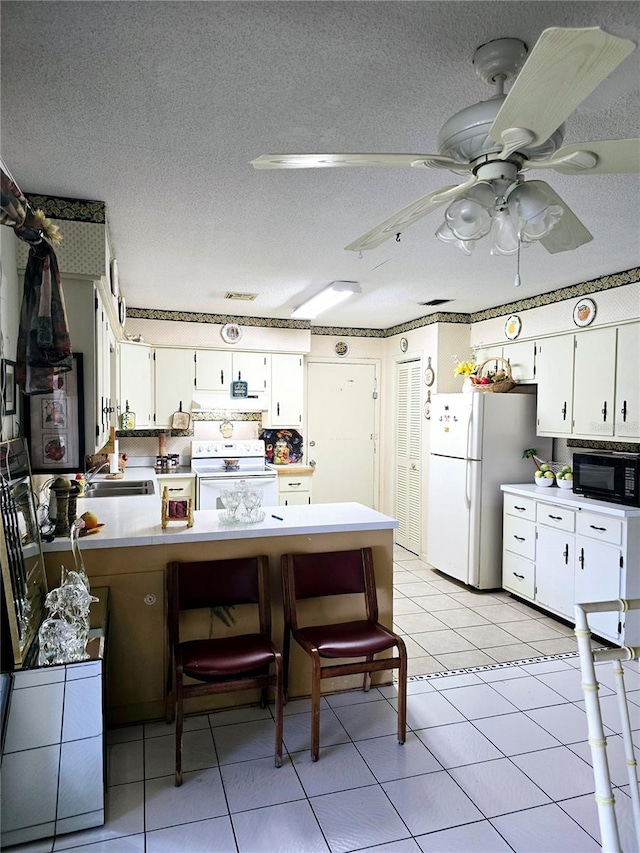 kitchen featuring white cabinets, light tile patterned floors, white appliances, and a textured ceiling