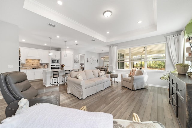 living room with a tray ceiling, crown molding, and light hardwood / wood-style floors