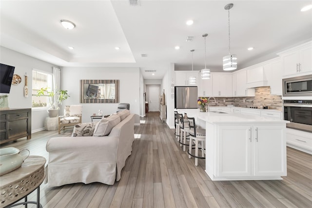 living room featuring a tray ceiling, sink, and light hardwood / wood-style floors