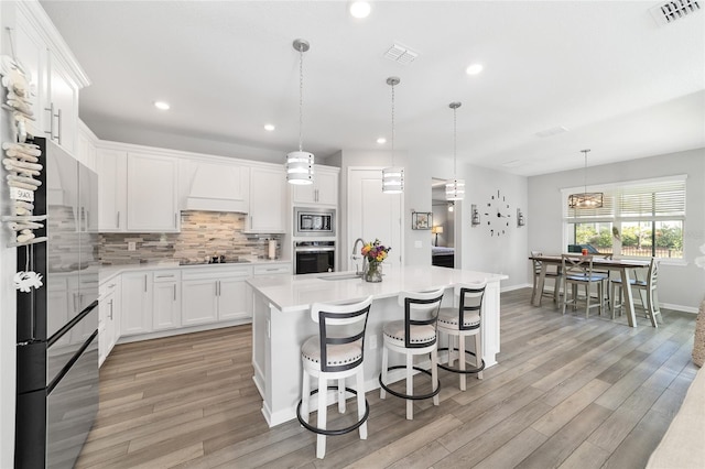 kitchen featuring stainless steel appliances, sink, decorative light fixtures, white cabinets, and an island with sink