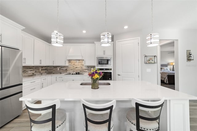 kitchen featuring a kitchen island with sink, white cabinets, hanging light fixtures, and appliances with stainless steel finishes