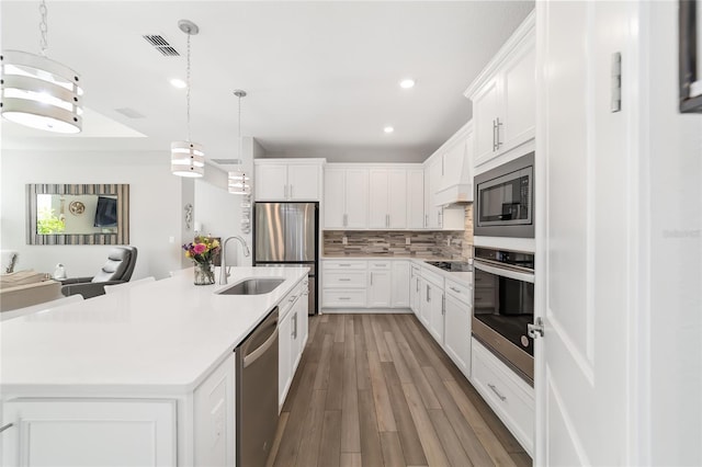 kitchen with white cabinetry, sink, stainless steel appliances, tasteful backsplash, and a kitchen island with sink