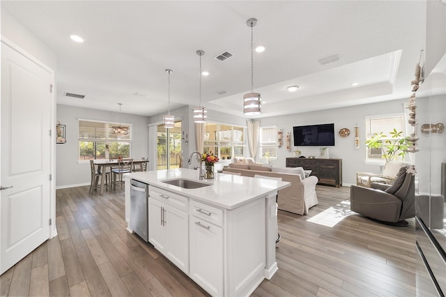 kitchen featuring white cabinets, a tray ceiling, dishwasher, hanging light fixtures, and an island with sink