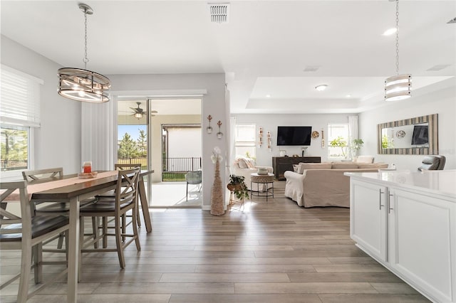 dining area featuring a notable chandelier, a raised ceiling, and light hardwood / wood-style flooring