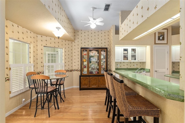 interior space with white cabinets, ceiling fan, a kitchen breakfast bar, and light wood-type flooring