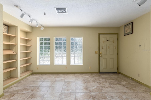 spare room featuring built in shelves, a textured ceiling, track lighting, and light tile patterned flooring